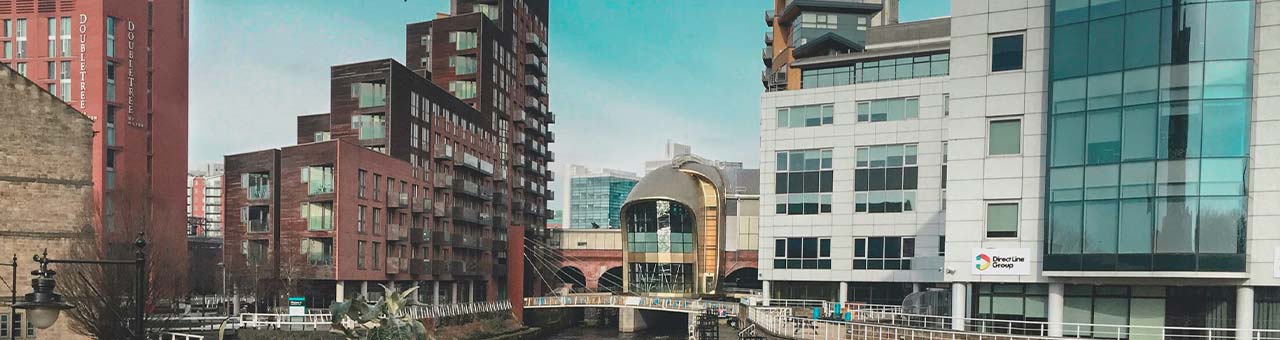 Buildings surrounding a canal in Leeds with a canal boat floating through the canal.